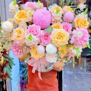 Người giao hoa đang cầm bó hoa rực rỡ với sắc vàng, hồng, trắng tại shop hoa tươi gần chợ