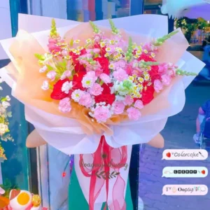 Bó hoa tươi cắm sẵn với tone hồng cam pastel, được trưng bày trước cửa shop – phù hợp tặng sinh nhật, lễ, chúc mừng.