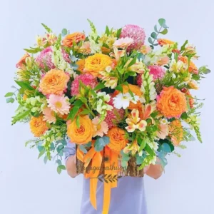 Một người đang ôm giỏ hoa cắm sẵn màu cam – trắng rực rỡ, đại diện cho sản phẩm hoa cắm sẵn gần đây tại Hoa Gửi Yêu Thương.